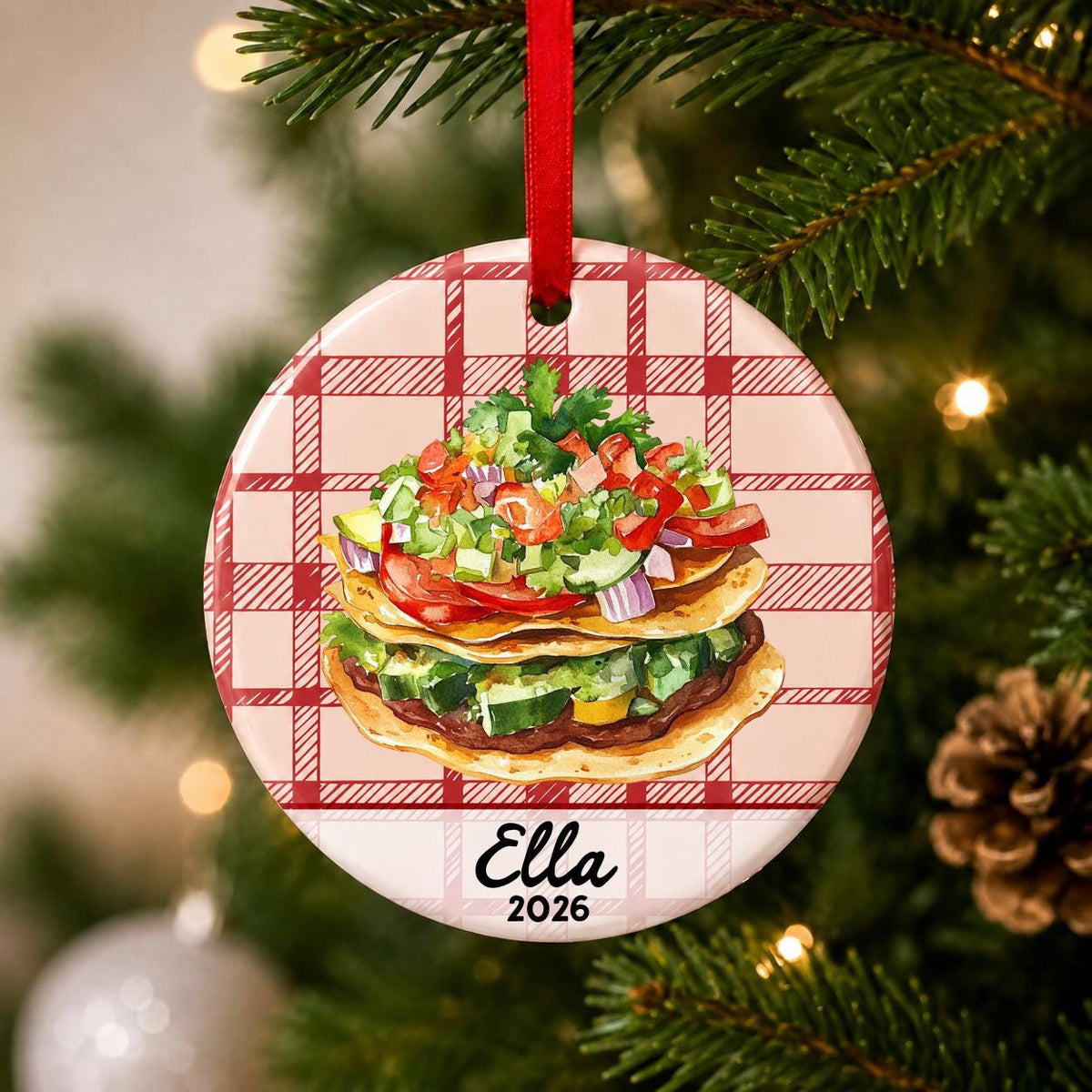 Close-up of the personalized tostada ceramic ornament with name and year on red plaid hanging on a Christmas tree