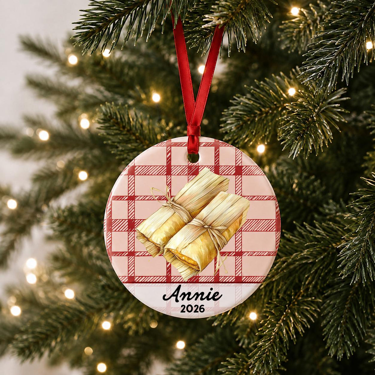 Personalized tamale ceramic ornament with name and year on red plaid hanging on a lit Christmas tree