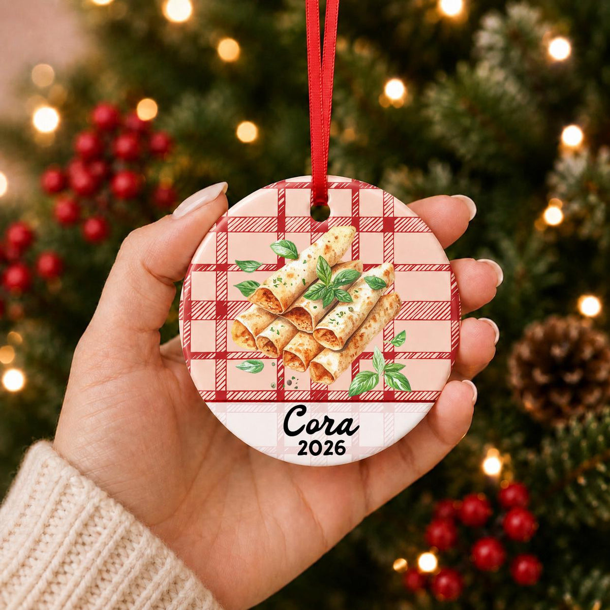Hand holding the personalized taquito ceramic ornament with name and year on red plaid in front of a Christmas tree