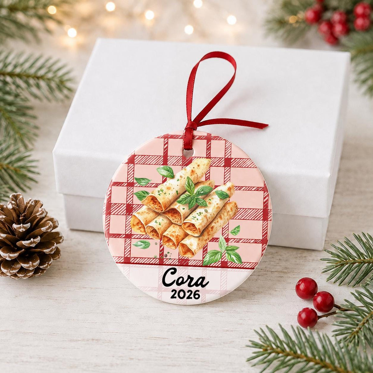 Personalized taquito ceramic ornament with name and year on red plaid in front of a white gift box with pinecones and red berries
