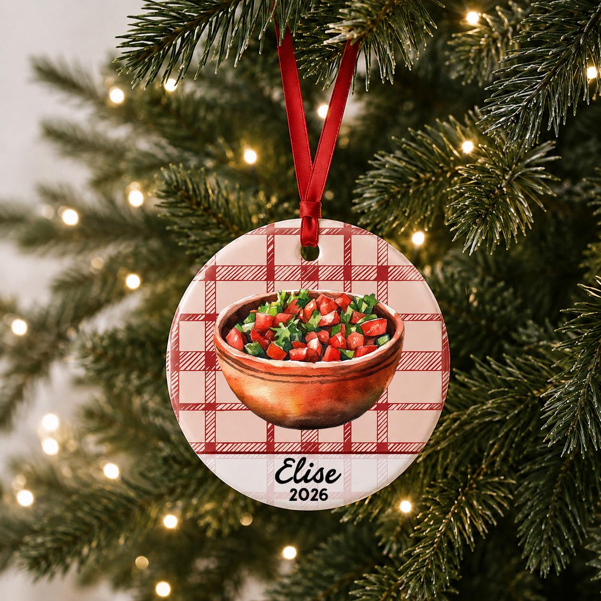 Personalized pico de gallo ceramic ornament with name and year on red plaid hanging on a lit Christmas tree