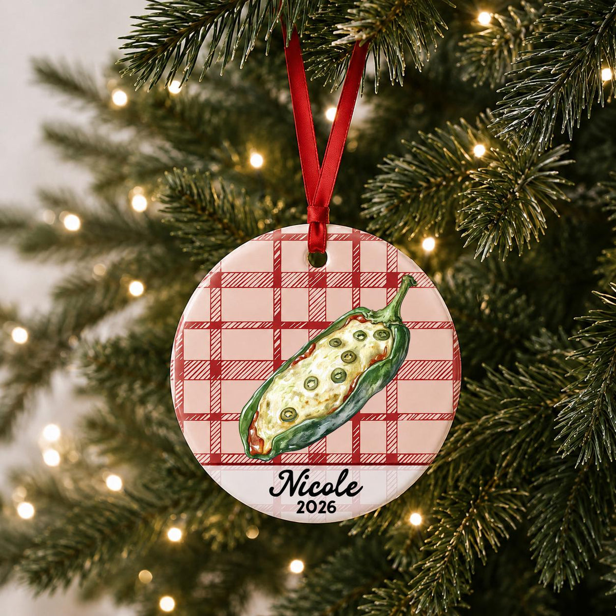 Personalized chile relleno ceramic ornament with name and year on red plaid hanging on a lit Christmas tree