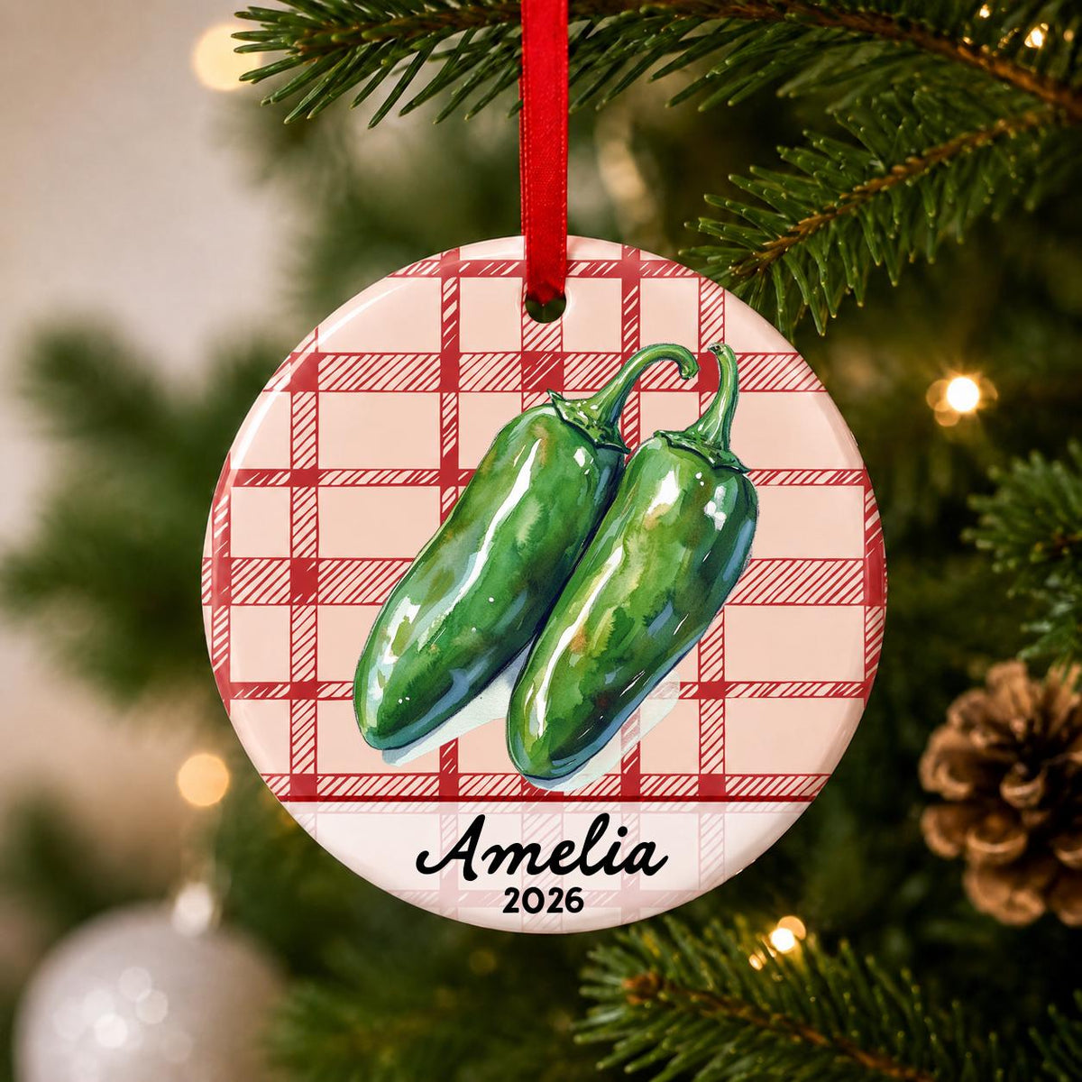 Close-up of the personalized jalapeño ceramic ornament with name and year on red plaid hanging on a Christmas tree