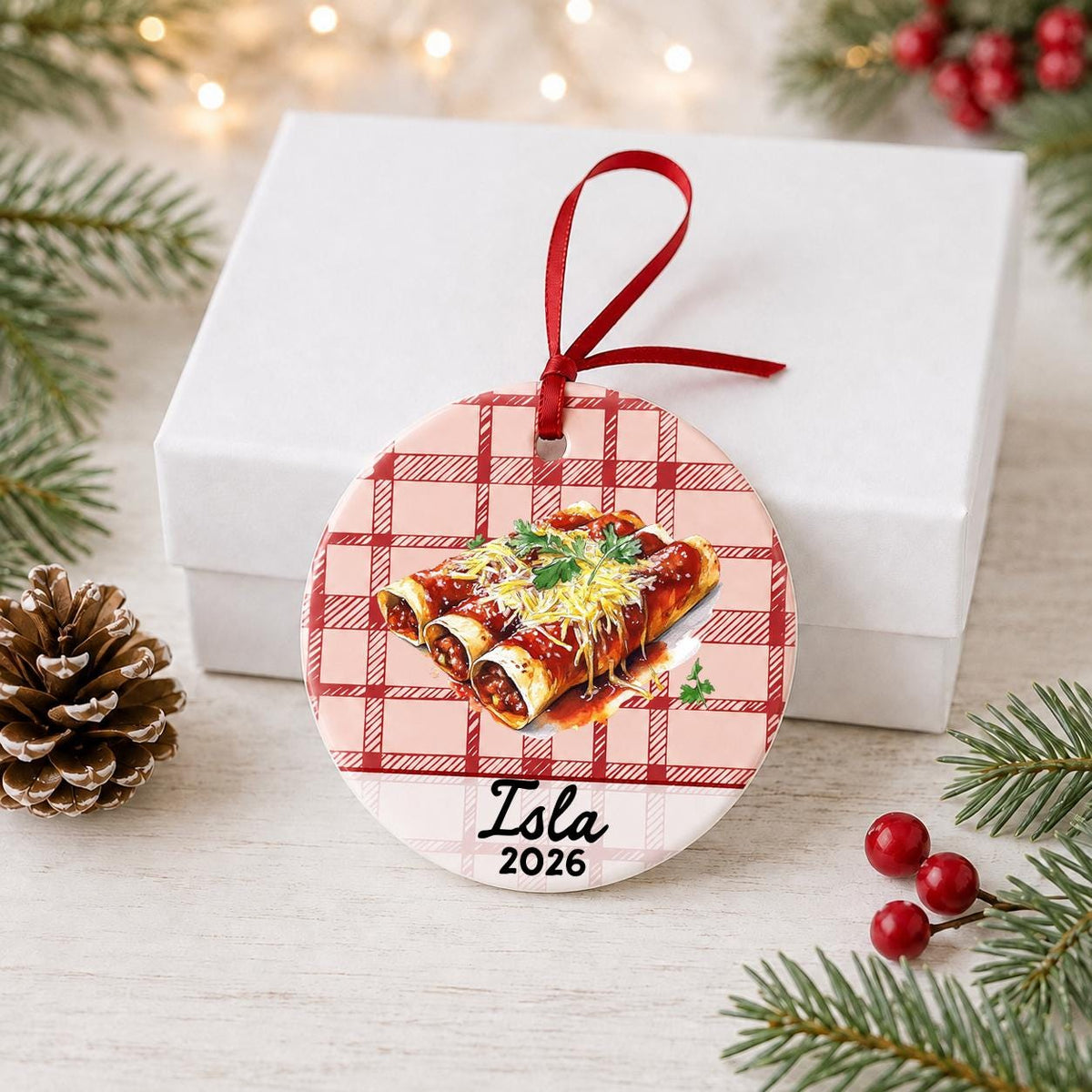 Personalized enchilada ceramic ornament with name and year on red plaid in front of a white gift box with pinecones and red berries