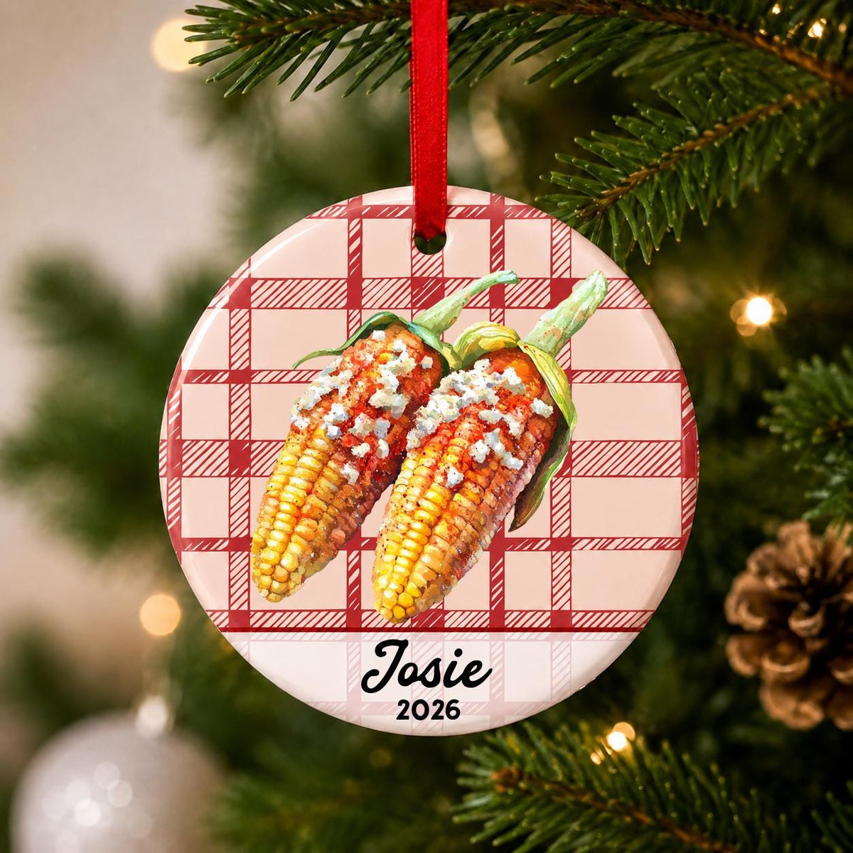 Close-up of the personalized Mexican street corn ceramic ornament with name and year on red plaid hanging on a Christmas tree