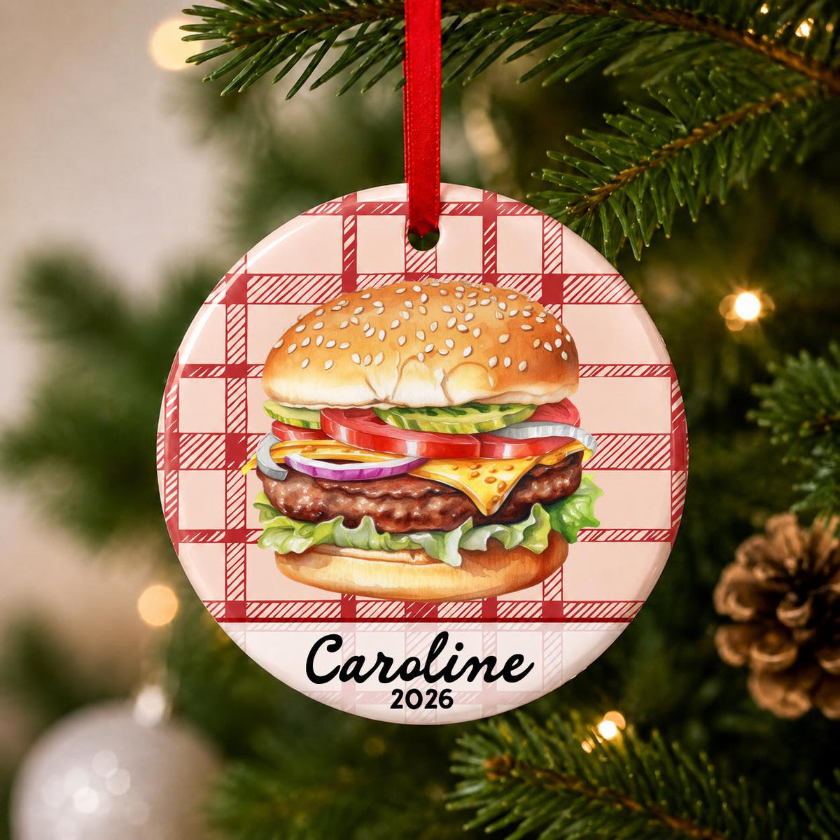 Close-up of the personalized cheeseburger ceramic ornament with name and year on red plaid hanging on a Christmas tree