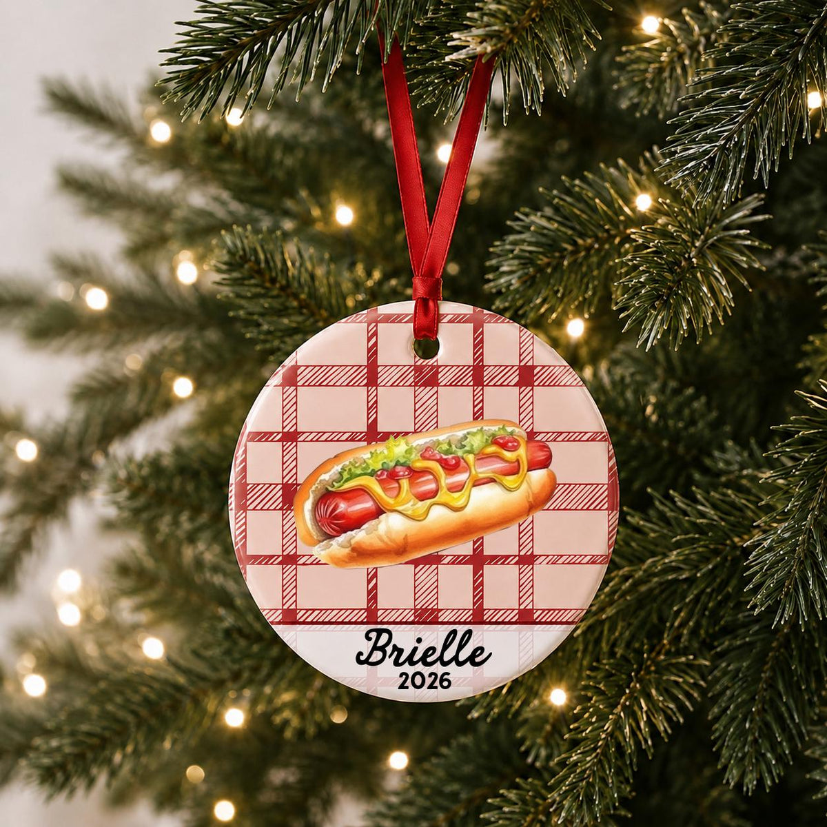 Personalized hot dog ceramic ornament with name and year on red plaid hanging on a lit Christmas tree