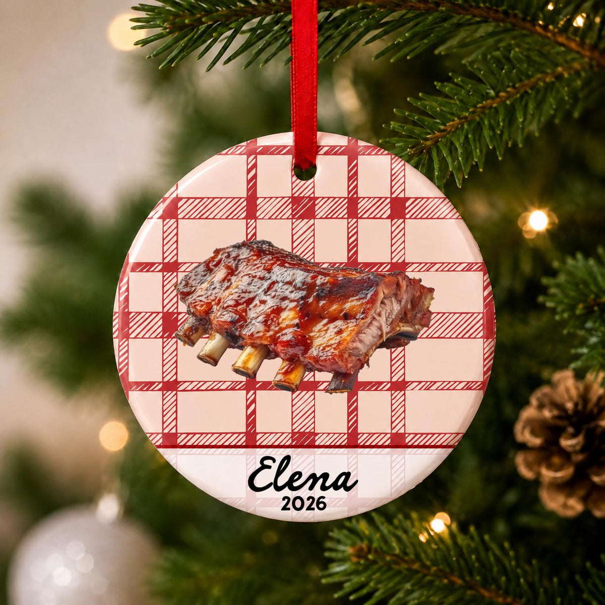 Close-up of the personalized BBQ ribs ceramic ornament with name and year on red plaid hanging on a Christmas tree