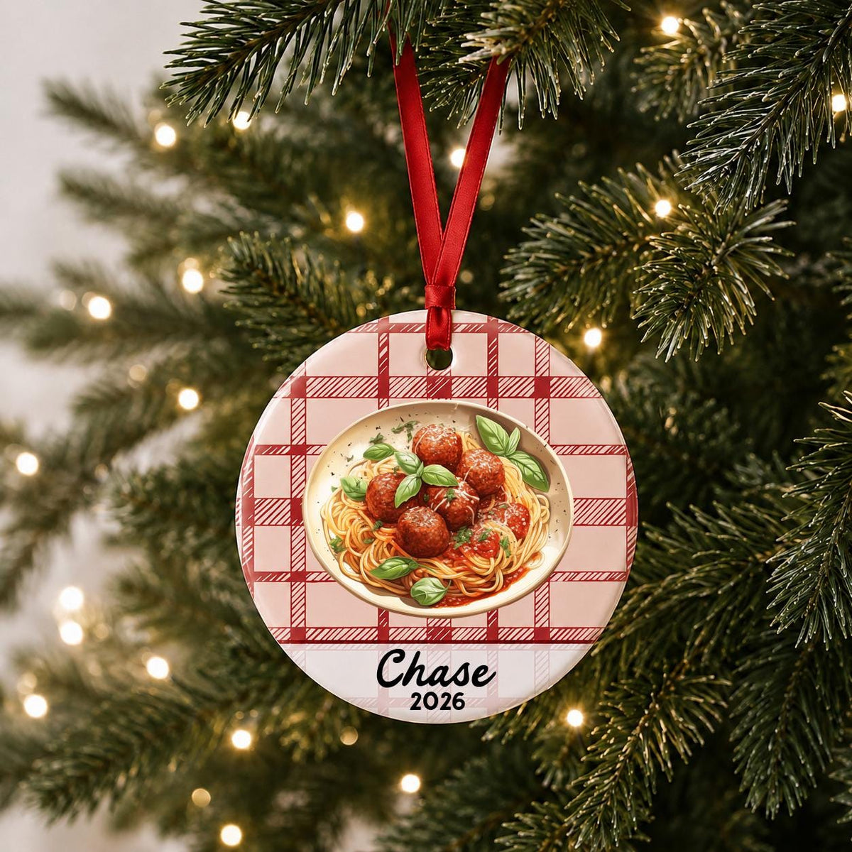 Personalized spaghetti and meatballs ceramic ornament with name and year on red plaid hanging on a lit Christmas tree
