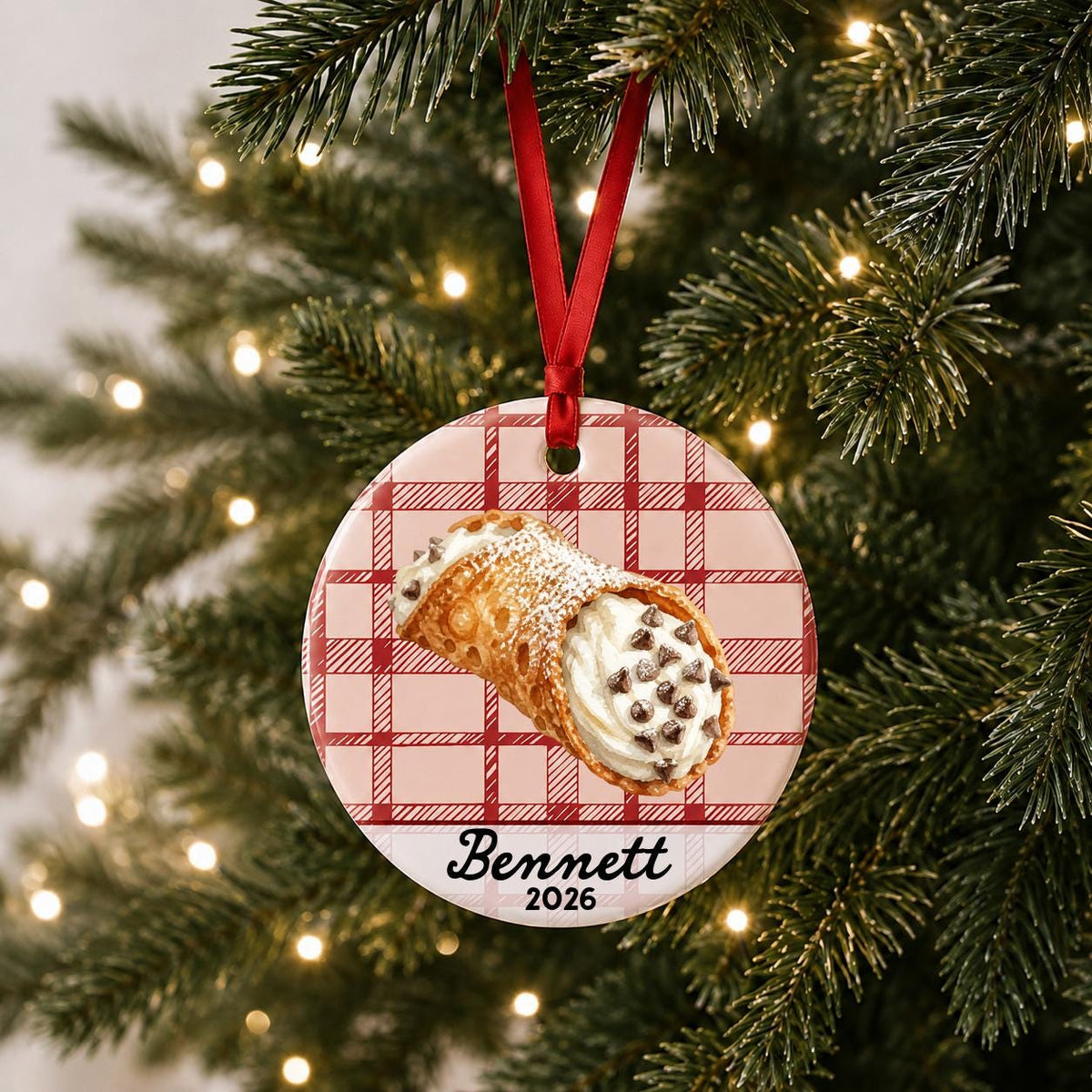 Personalized cannoli ceramic ornament with name and year on red plaid hanging on a lit Christmas tree