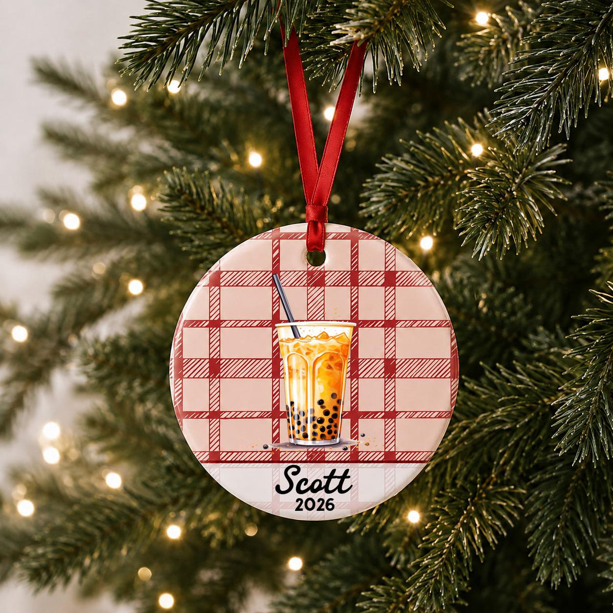 Personalized boba ceramic ornament with name and year on red plaid hanging on a lit Christmas tree