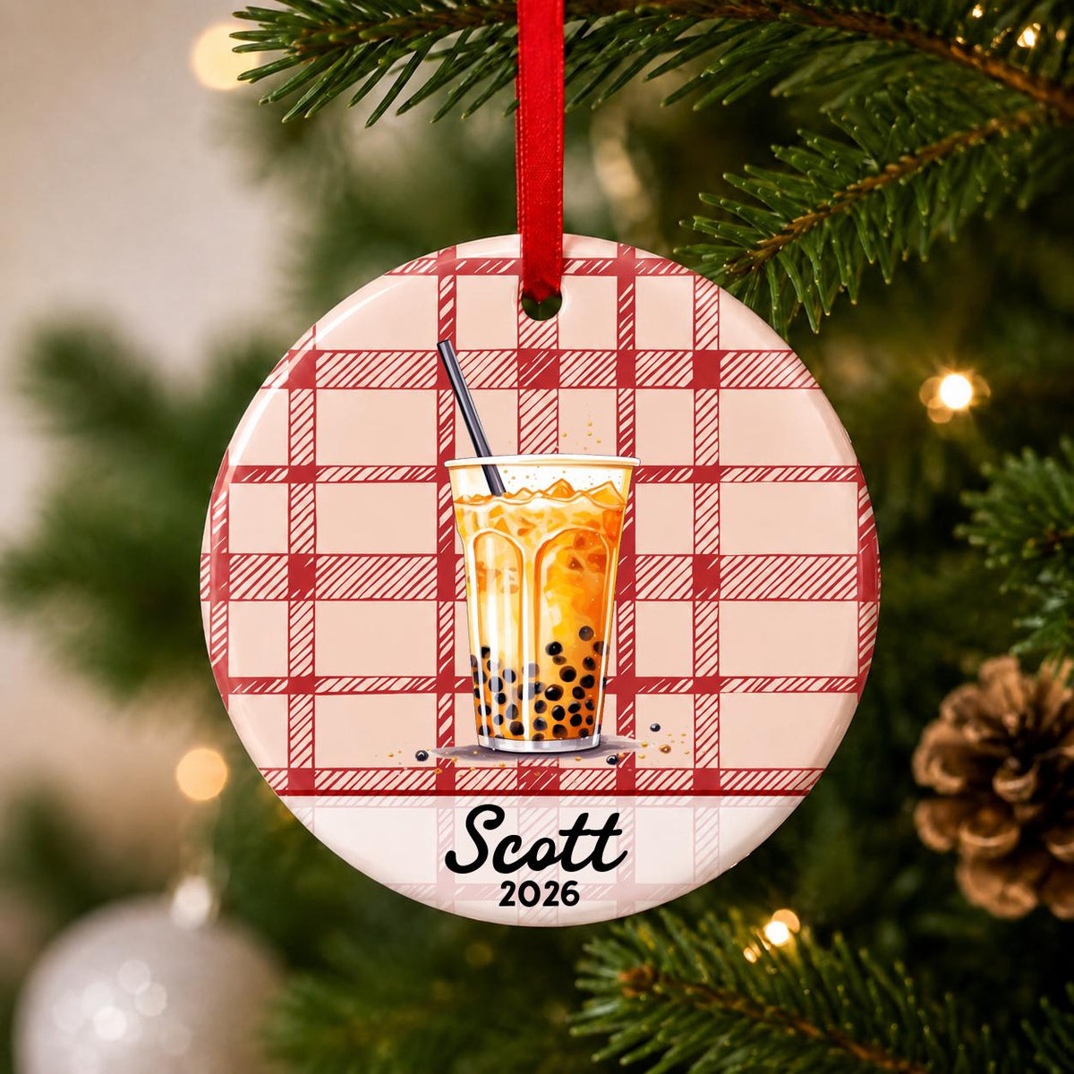 Close-up of the personalized boba ceramic ornament with name and year on red plaid hanging on a Christmas tree
