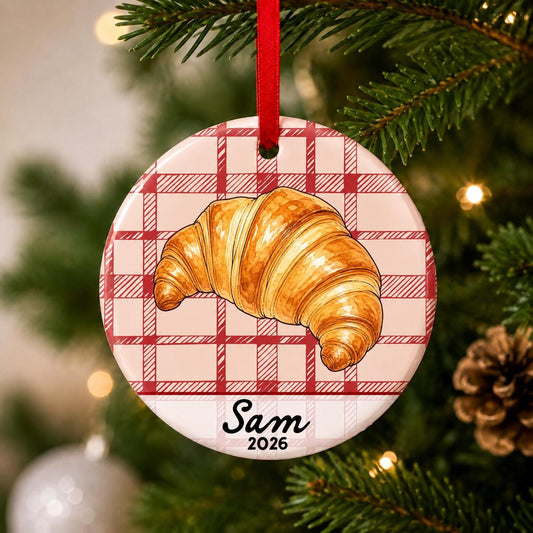 Close-up of the personalized croissant ceramic ornament with name and year on red plaid hanging on a Christmas tree