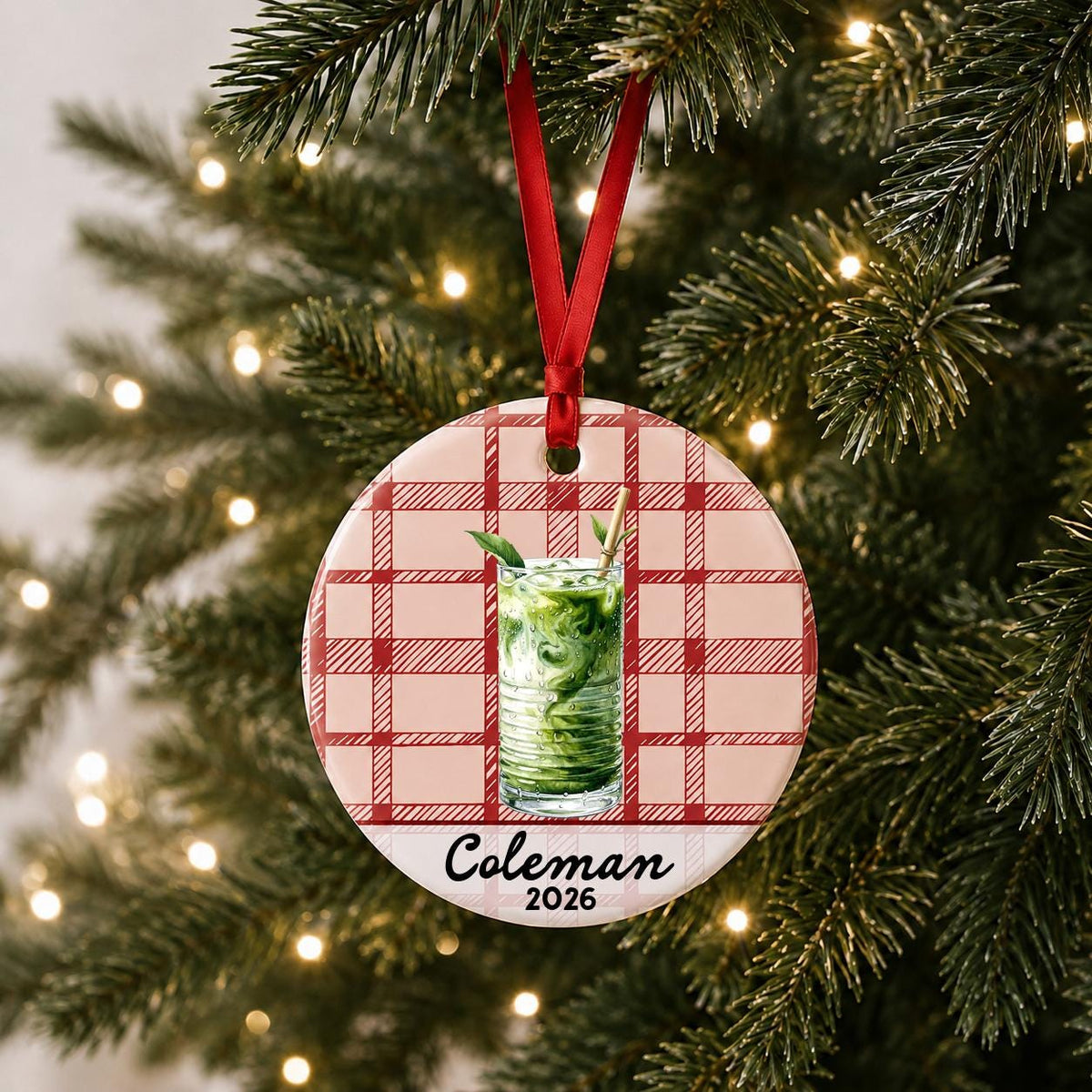 Personalized iced matcha ceramic ornament with name and year on red plaid hanging on a lit Christmas tree