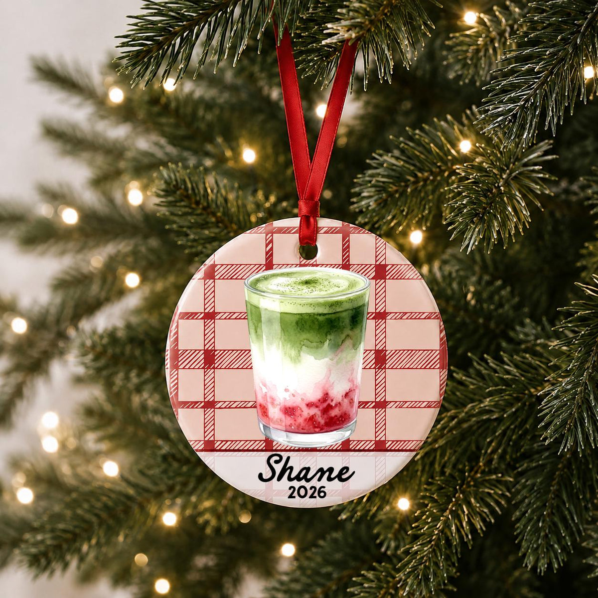 Personalized strawberry matcha latte ceramic ornament with name and year on red plaid hanging on a lit Christmas tree