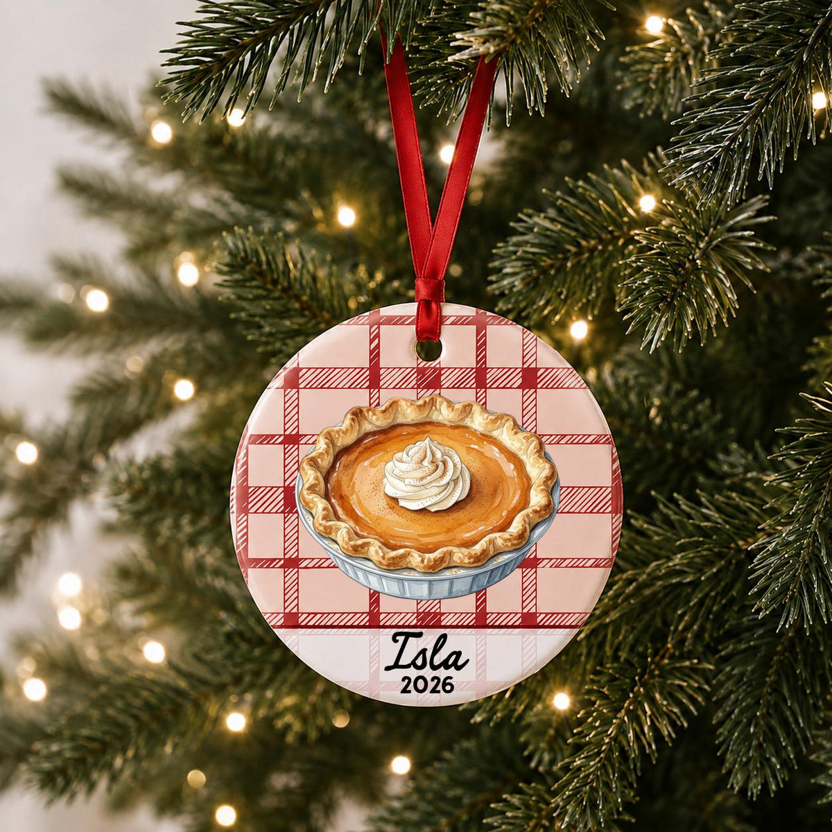 Personalized pumpkin pie ceramic ornament with name and year on red plaid hanging on a lit Christmas tree