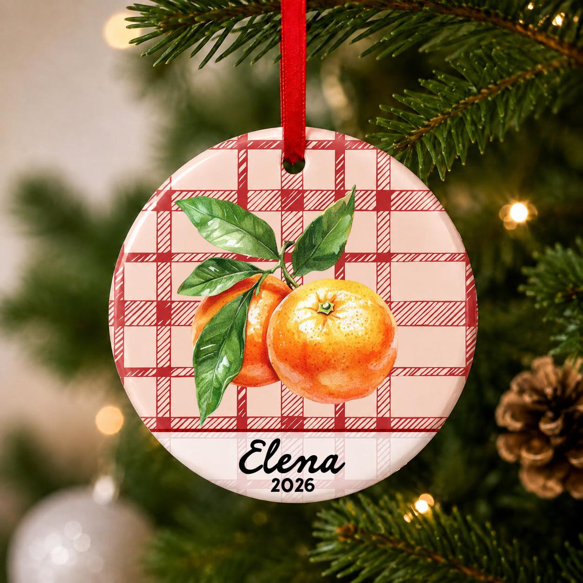 Close-up of the personalized clementine ceramic ornament with name and year on red plaid hanging on a Christmas tree