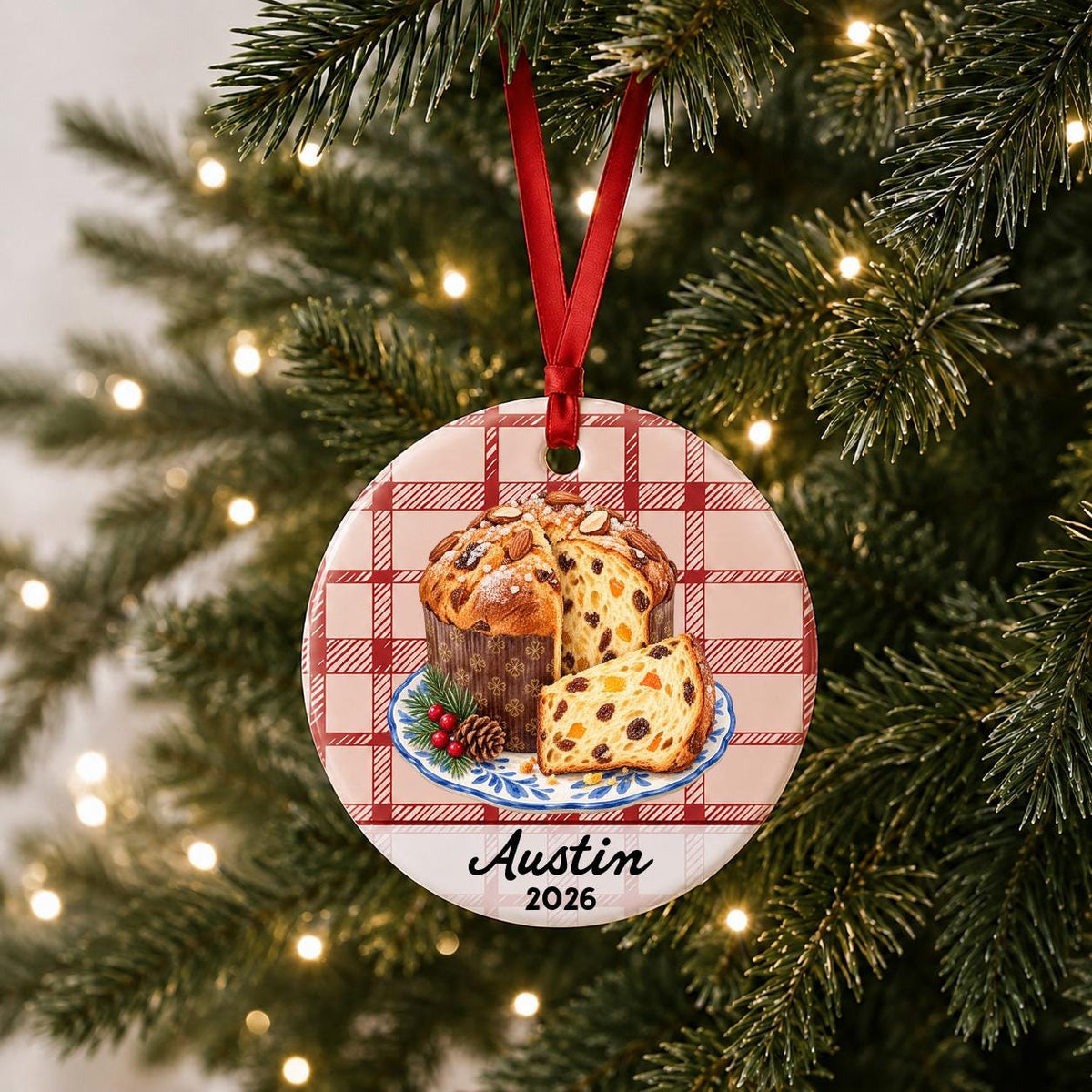 Personalized panettone ceramic ornament with name and year on red plaid hanging on a lit Christmas tree