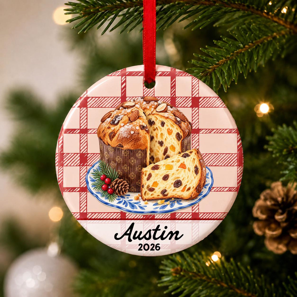 Close-up of the personalized panettone ceramic ornament with name and year on red plaid hanging on a Christmas tree