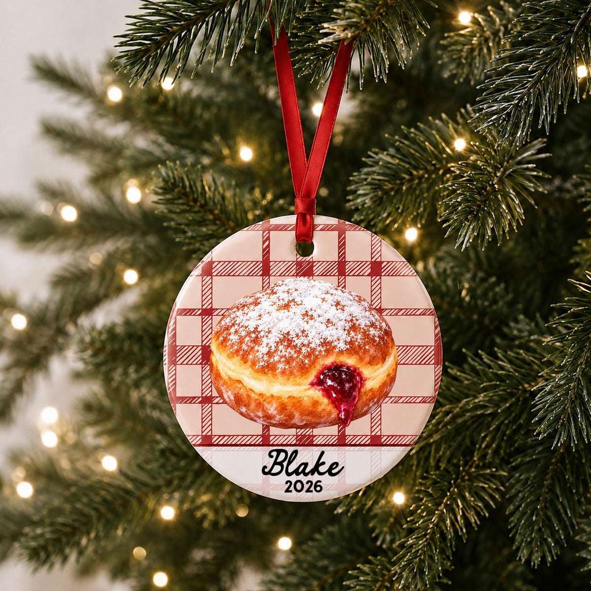 Personalized paczki ceramic ornament with name and year on red plaid hanging on a lit Christmas tree