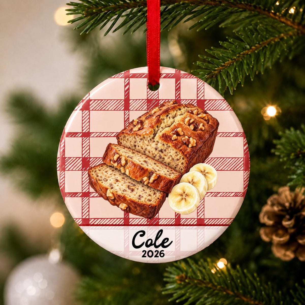 Close-up of the personalized banana bread ceramic ornament with name and year on red plaid hanging on a Christmas tree