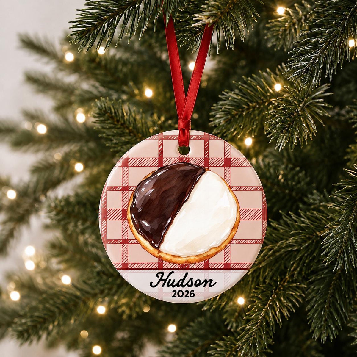 Personalized black and white cookie ceramic ornament with name and year on red plaid hanging on a lit Christmas tree