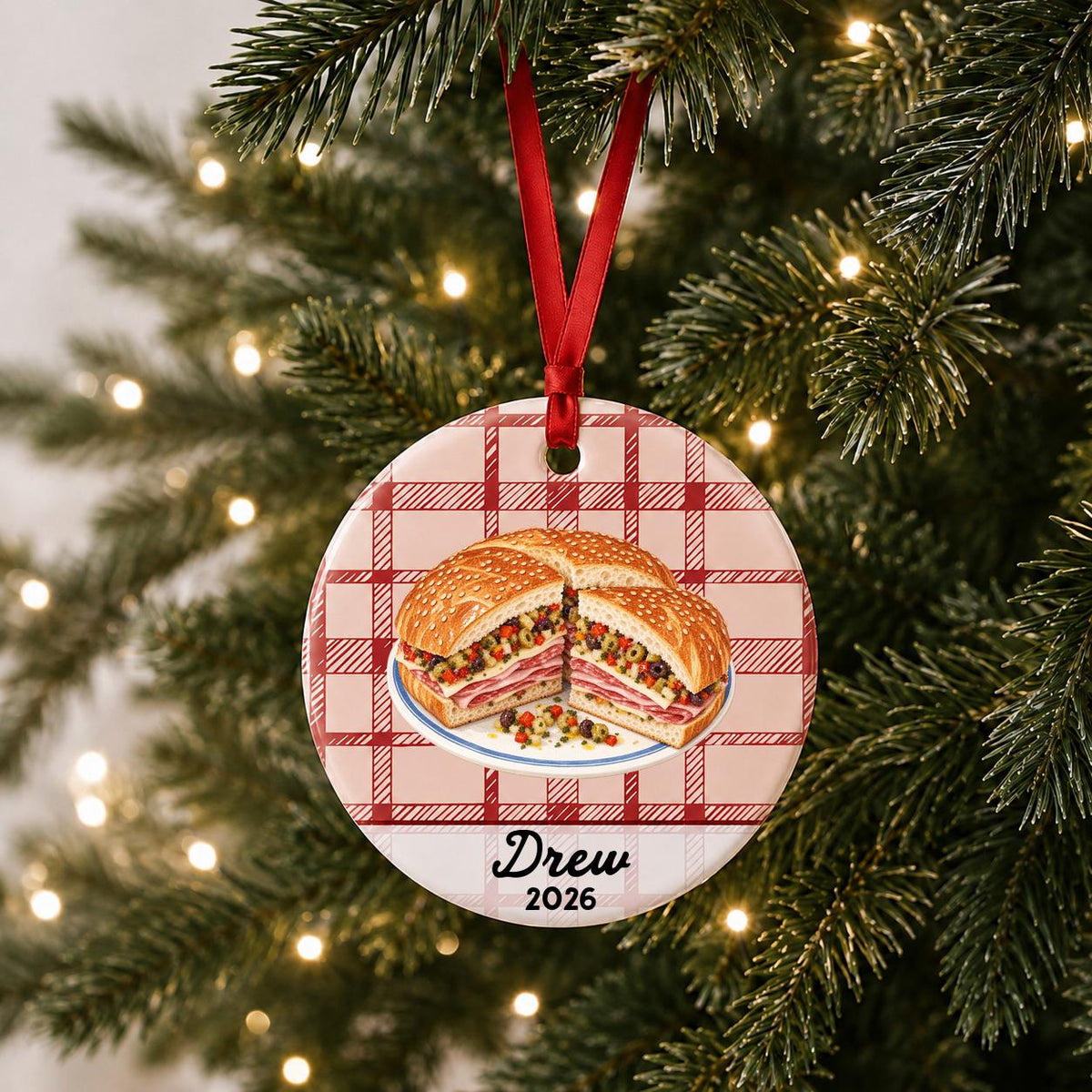 Personalized muffuletta ceramic ornament with name and year on red plaid hanging on a lit Christmas tree