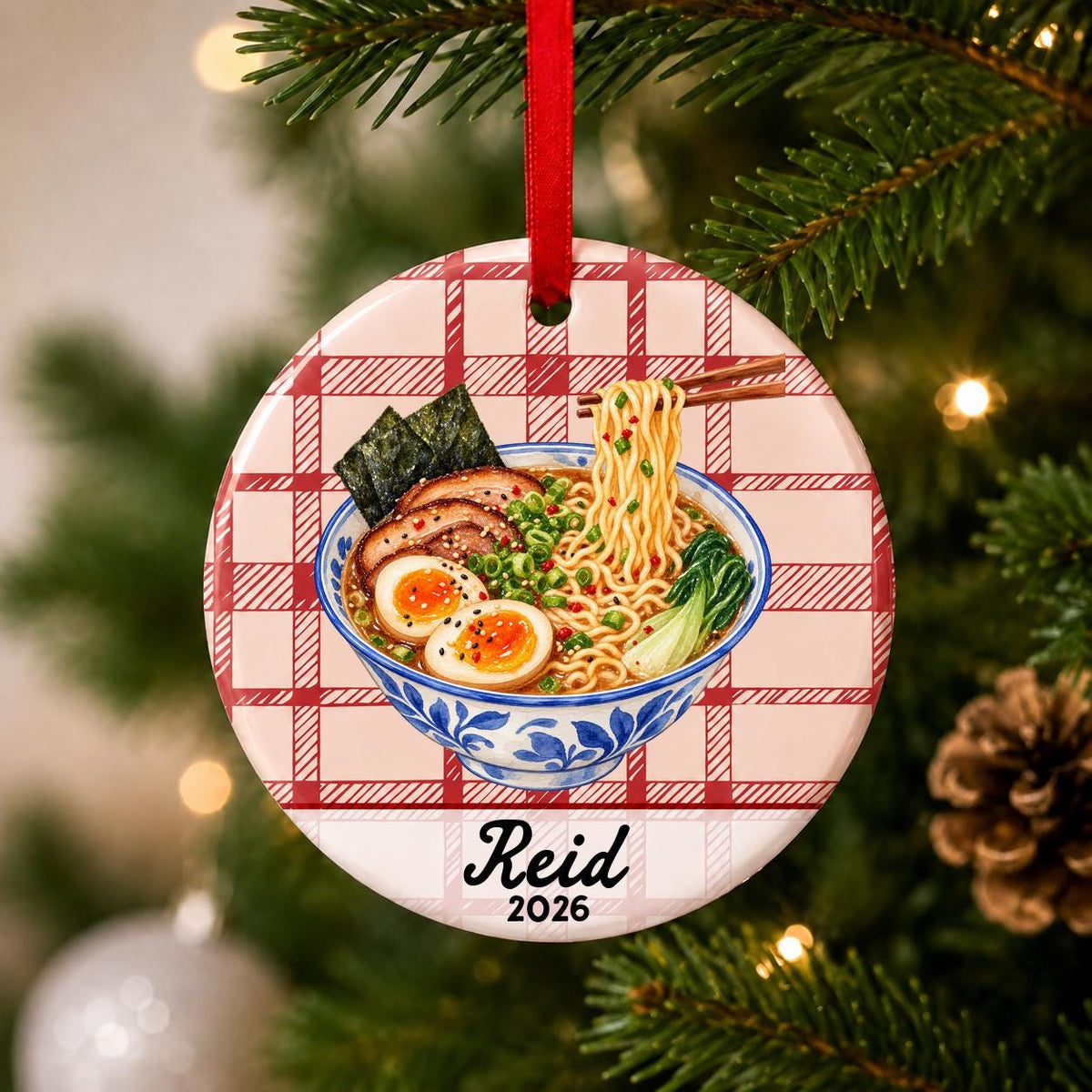 Close-up of the personalized ramen ceramic ornament with name and year on red plaid hanging on a Christmas tree