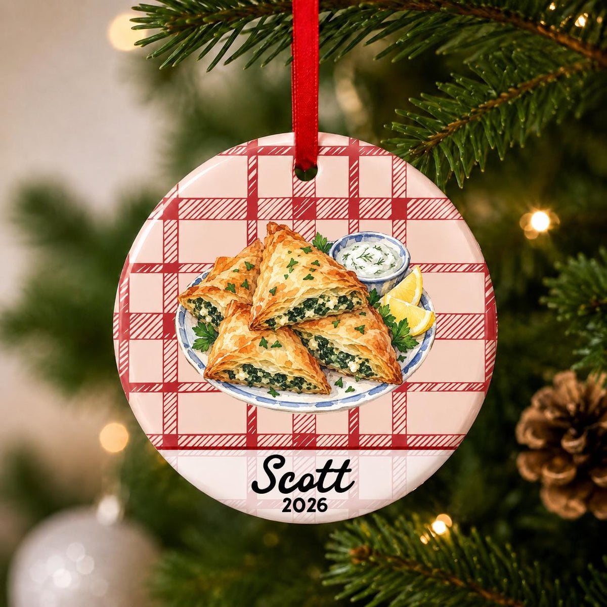 Close-up of the personalized spanakopita ceramic ornament with name and year on red plaid hanging on a Christmas tree