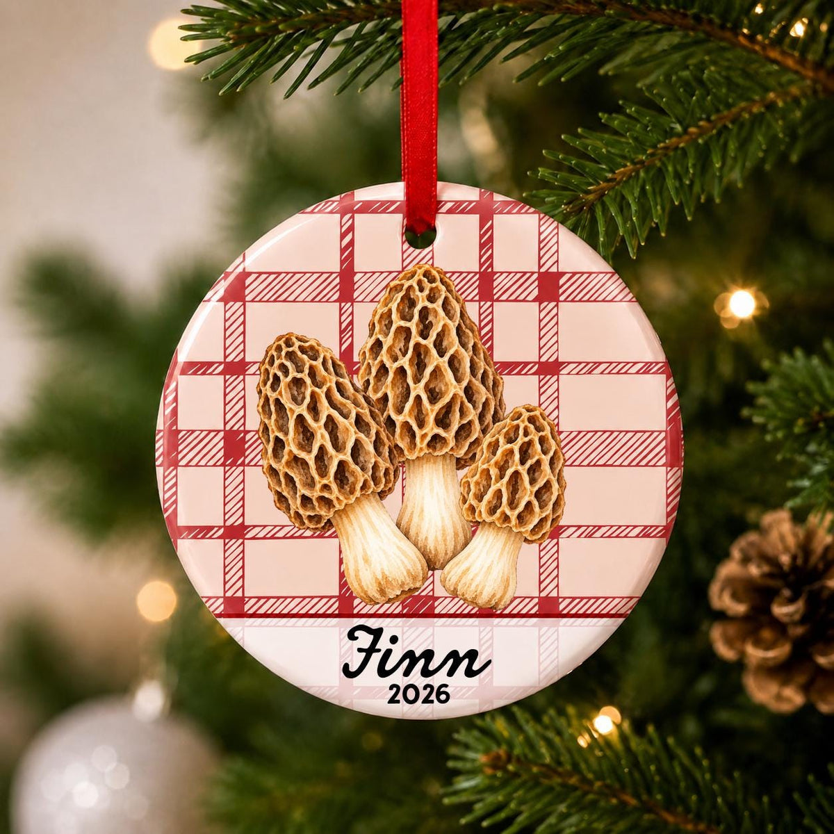 Close-up of the personalized morel mushrooms ceramic ornament with name and year on red plaid hanging on a Christmas tree