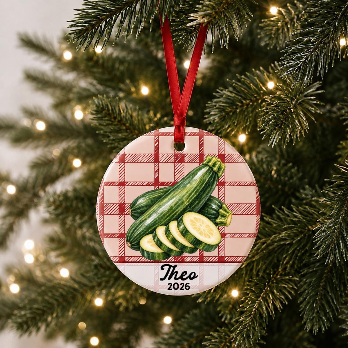 Personalized zucchini ceramic ornament with name and year on red plaid hanging on a lit Christmas tree