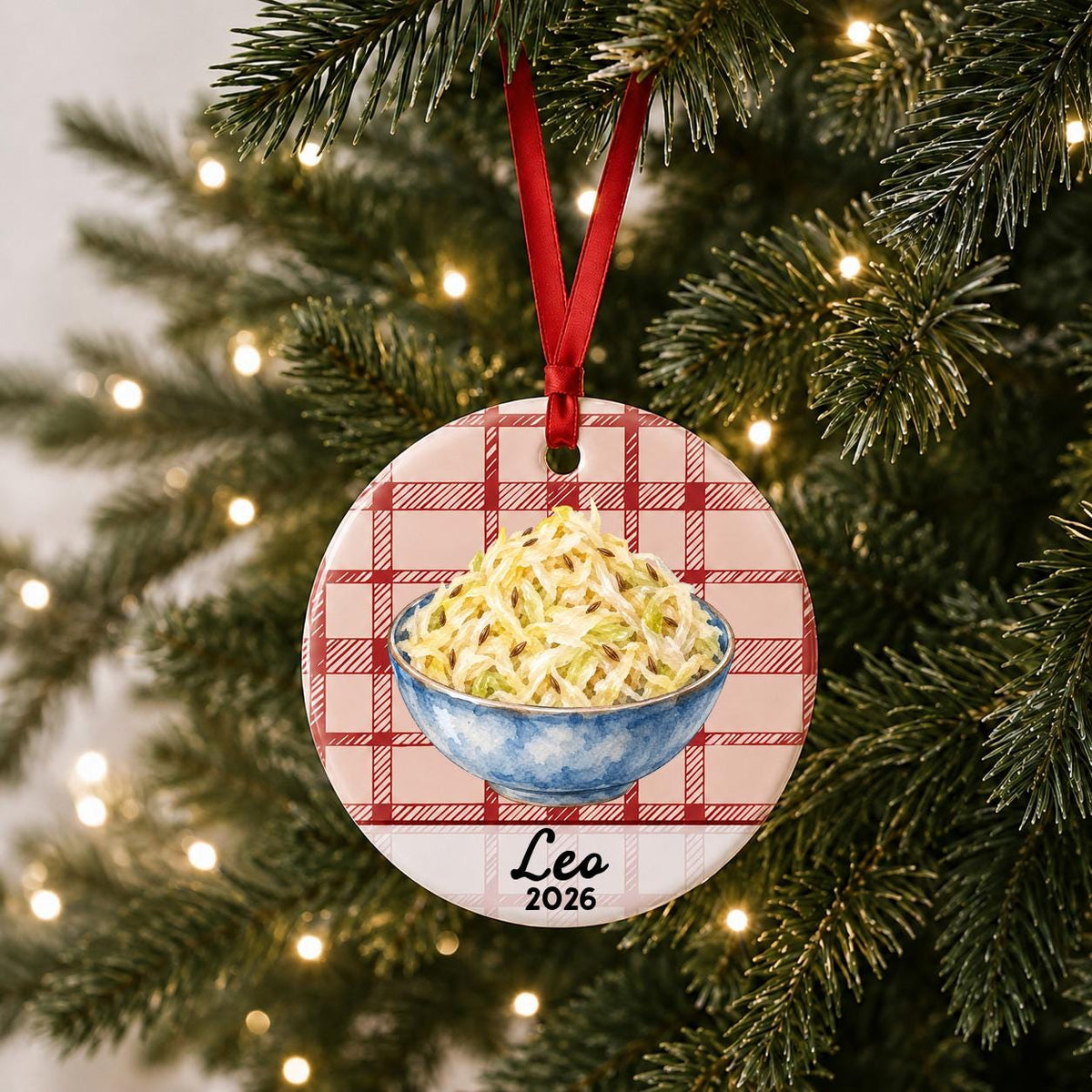 Personalized sauerkraut ceramic ornament with name and year on red plaid hanging on a lit Christmas tree