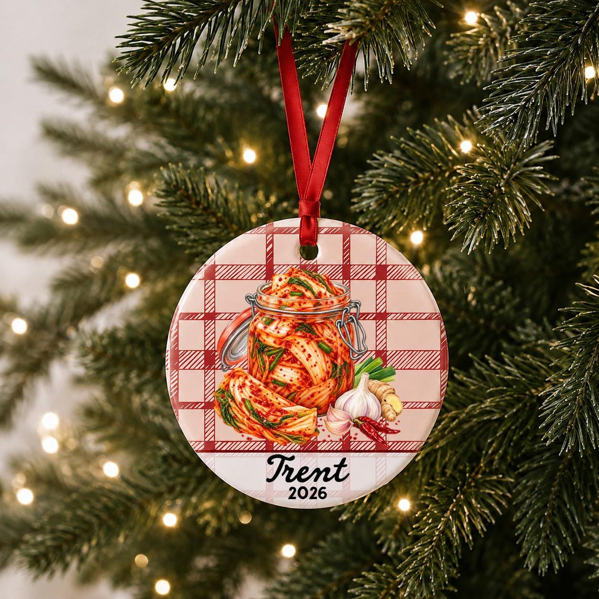 Personalized kimchi ceramic ornament with name and year on red plaid hanging on a lit Christmas tree