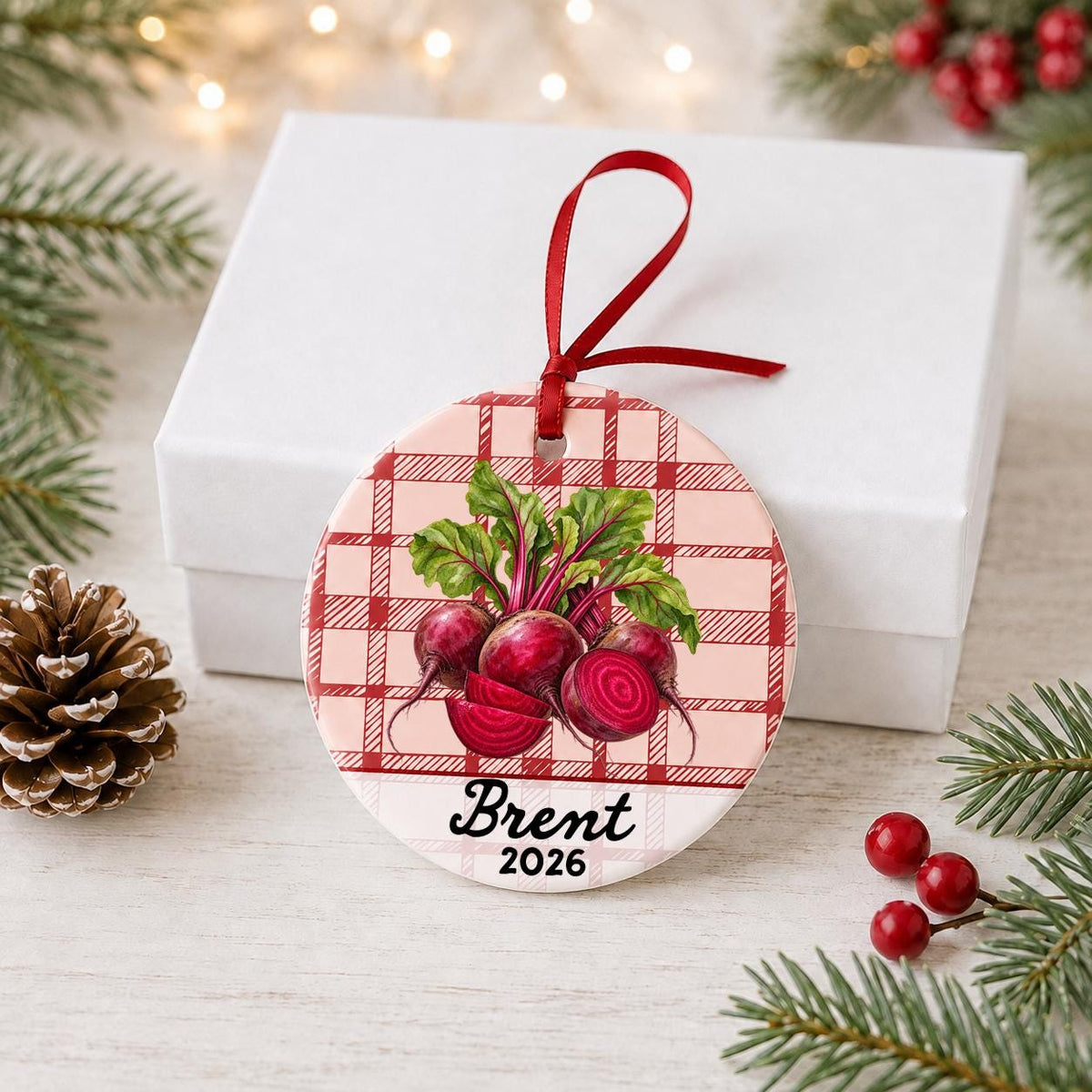 Personalized beets ceramic ornament with name and year on red plaid in front of a white gift box with pinecones and red berries