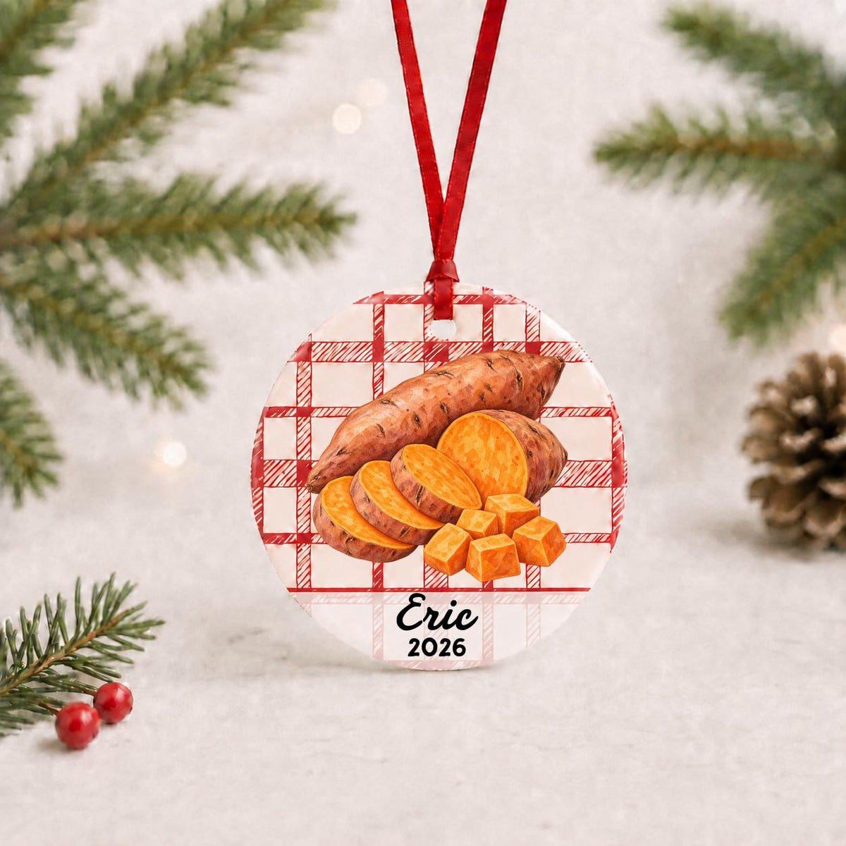 Personalized sweet potato ceramic ornament with name and year on red plaid with red ribbon on a white surface with pine branches and pinecones
