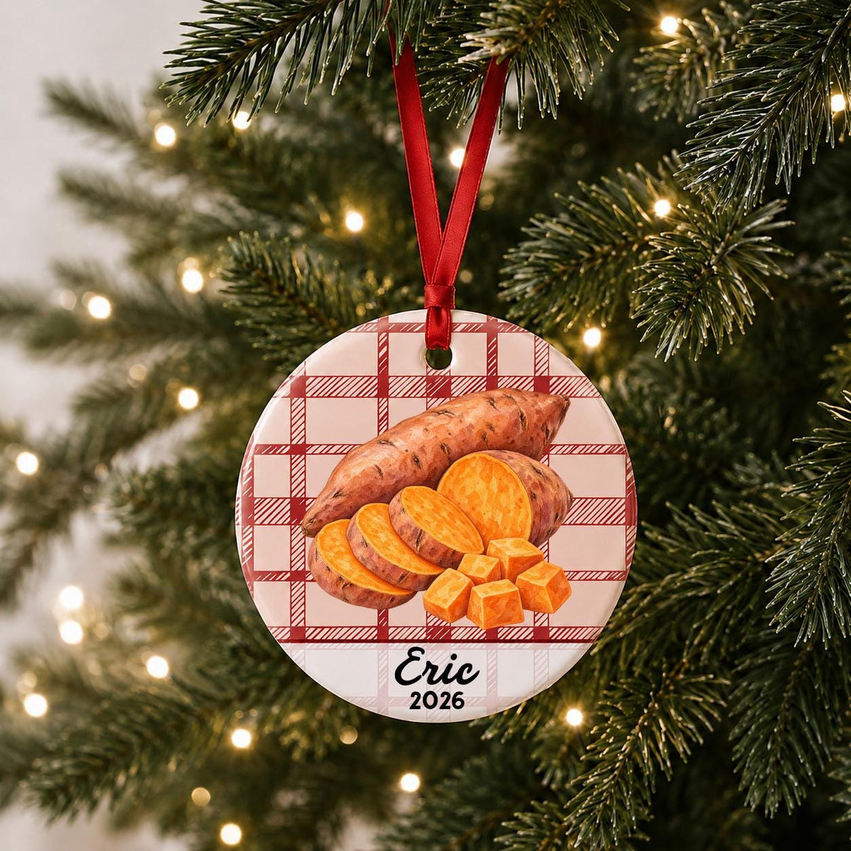 Personalized sweet potato ceramic ornament with name and year on red plaid hanging on a lit Christmas tree