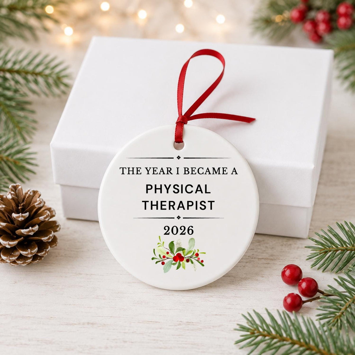 Physical Therapist 2026 ceramic ornament reading The Year I Became a Physical Therapist in front of a white gift box with pinecones and red berries