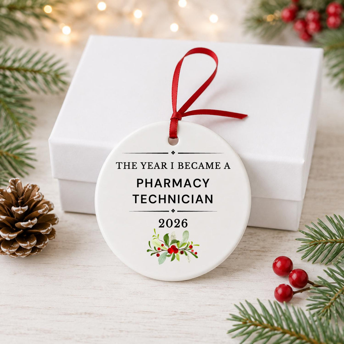 Pharmacy Technician 2026 ceramic ornament reading The Year I Became a Pharmacy Technician in front of a white gift box with pinecones and red berries