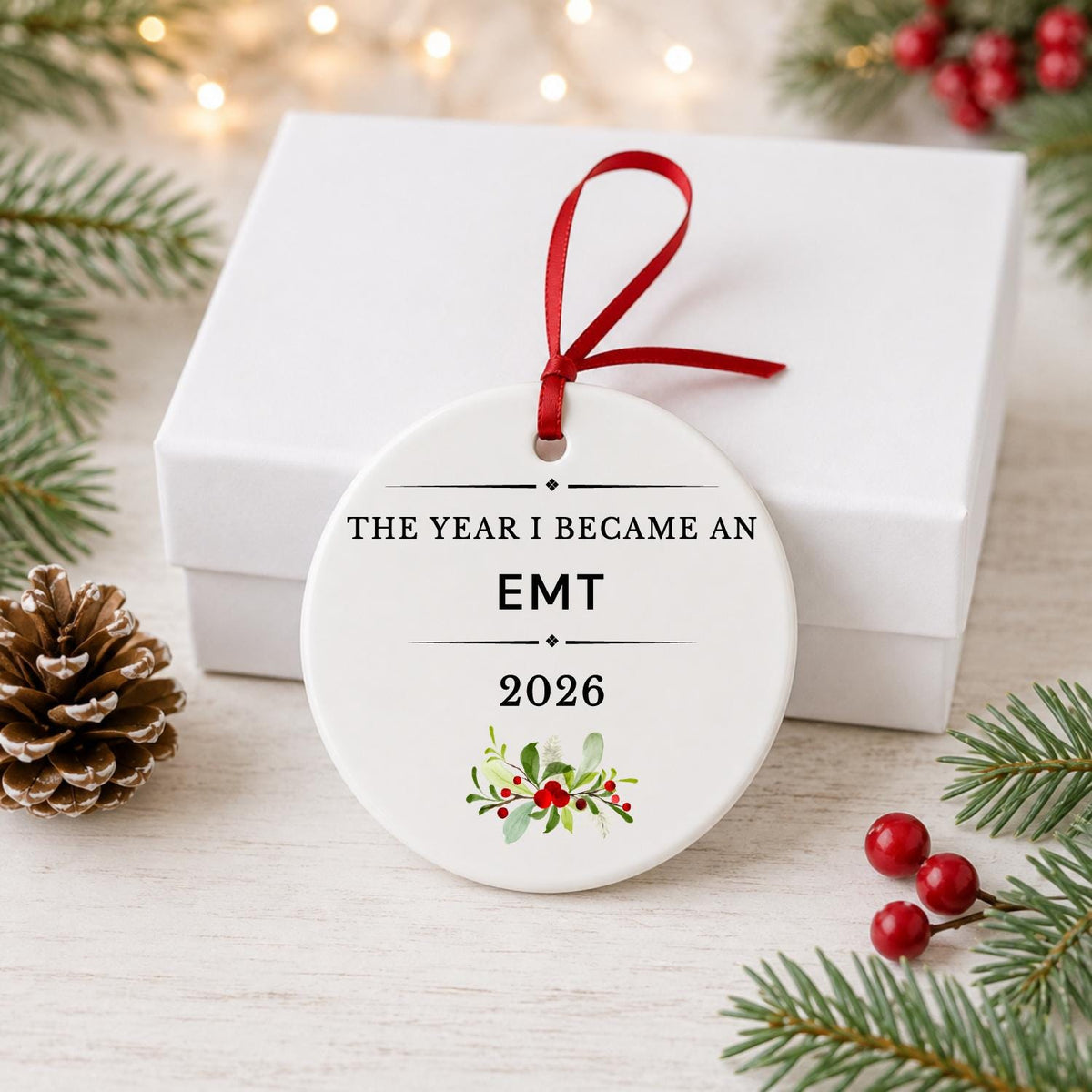 EMT 2026 ceramic ornament reading The Year I Became an EMT in front of a white gift box with pinecones and red berries