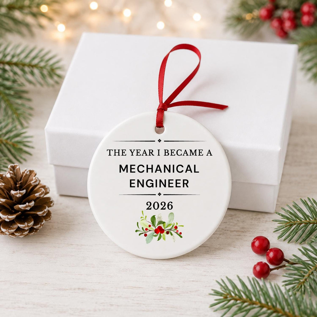 Mechanical Engineer 2026 ceramic ornament reading The Year I Became a Mechanical Engineer in front of a white gift box with pinecones and red berries