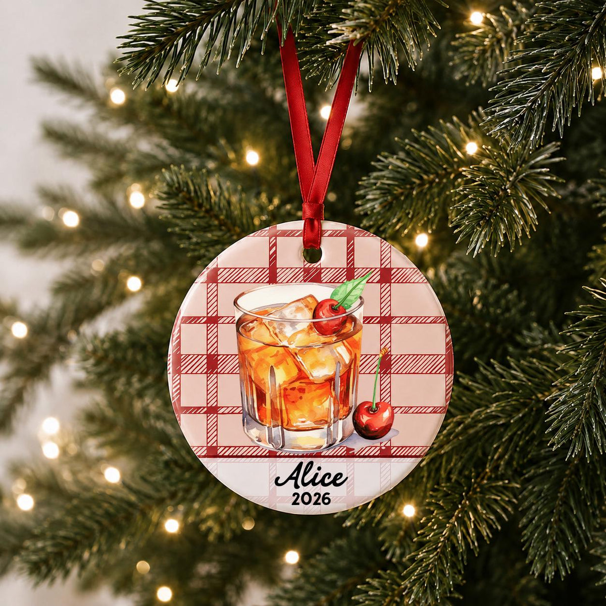 Personalized Old Fashioned cocktail ceramic ornament with name and year on red plaid hanging on a lit Christmas tree