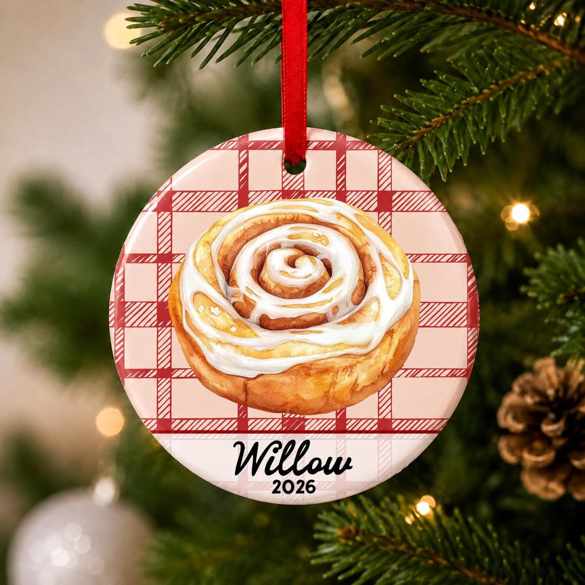Close-up of the personalized cinnamon roll ceramic ornament with name and year on red plaid hanging on a Christmas tree