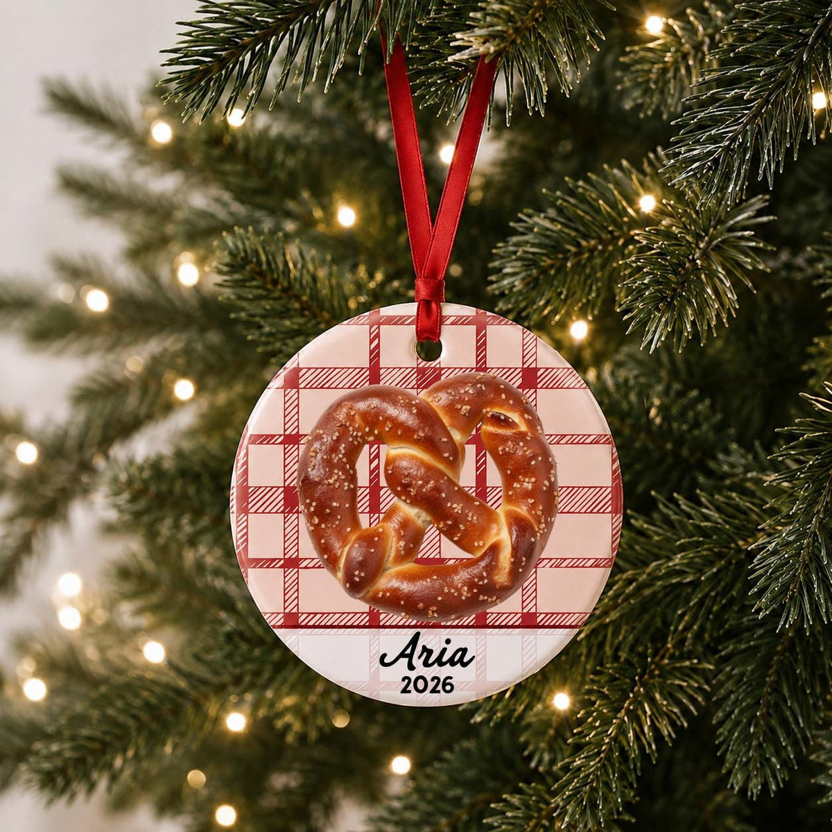 Personalized soft pretzel ceramic ornament with name and year on red plaid hanging on a lit Christmas tree