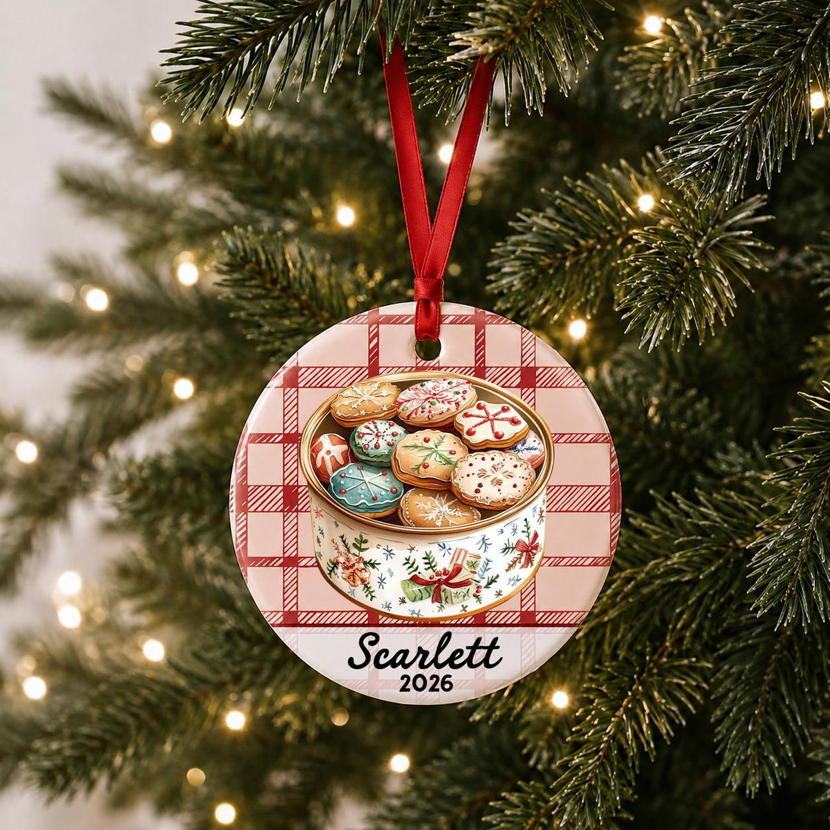 Personalized Christmas cookie tin ceramic ornament with name and year on red plaid hanging on a lit Christmas tree