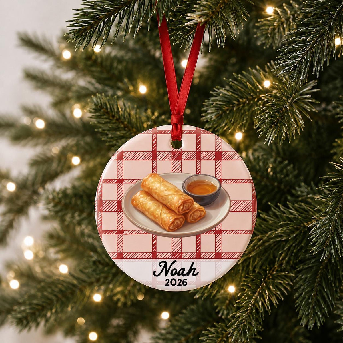 Personalized egg roll ceramic ornament with name and year on red plaid hanging on a lit Christmas tree
