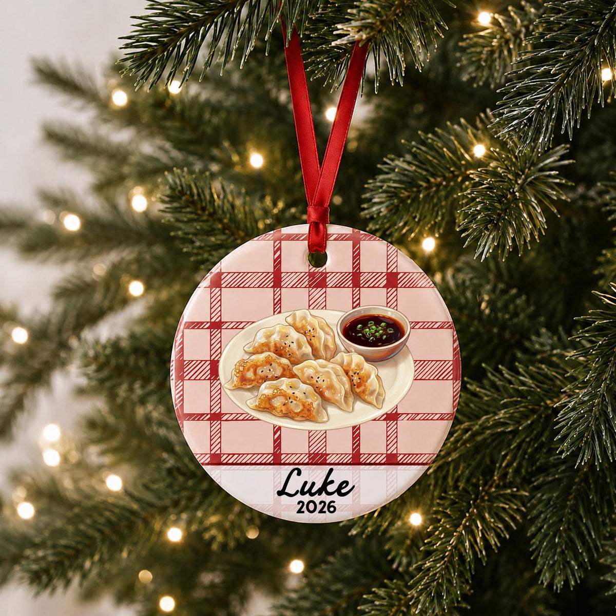 Personalized potsticker ceramic ornament with name and year on red plaid hanging on a lit Christmas tree