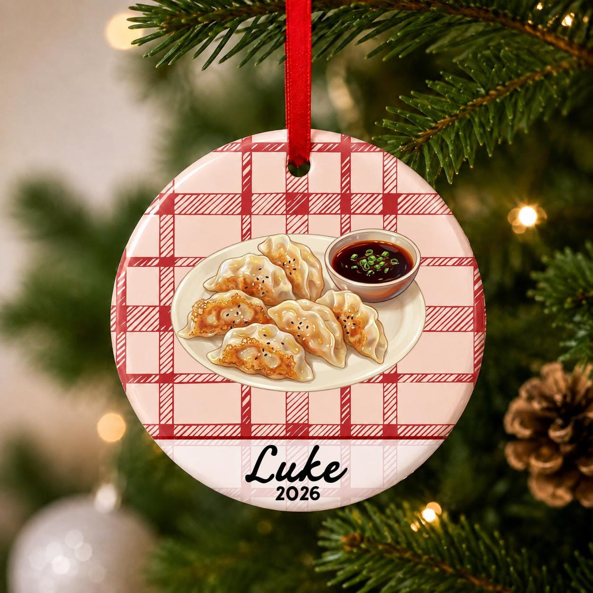 Close-up of the personalized potsticker ceramic ornament with name and year on red plaid hanging on a Christmas tree