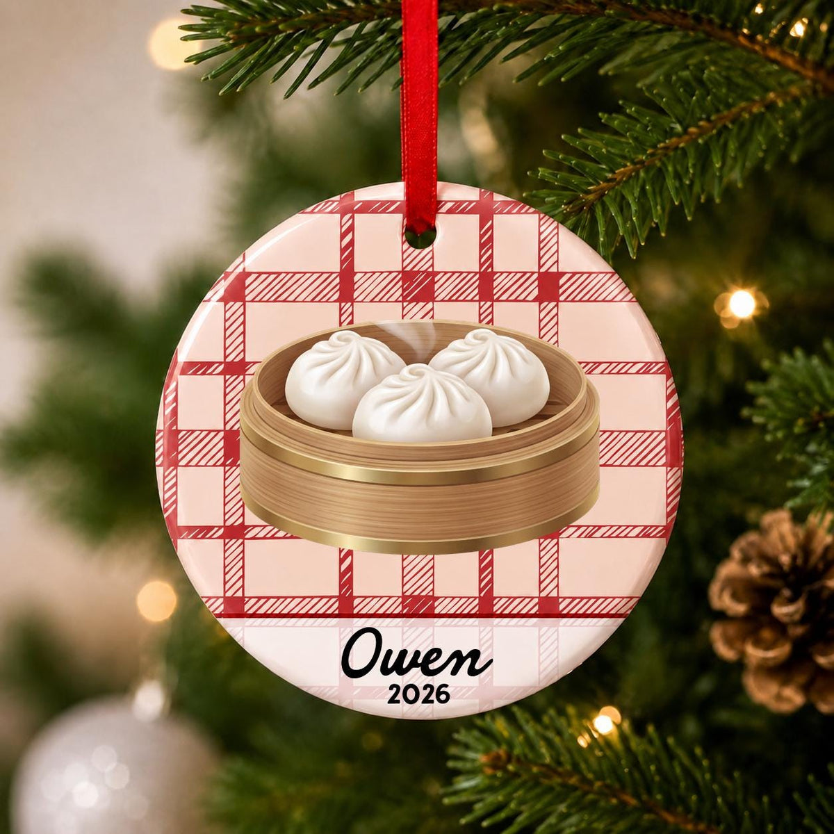 Close-up of the personalized soup dumpling ceramic ornament with name and year on red plaid hanging on a Christmas tree