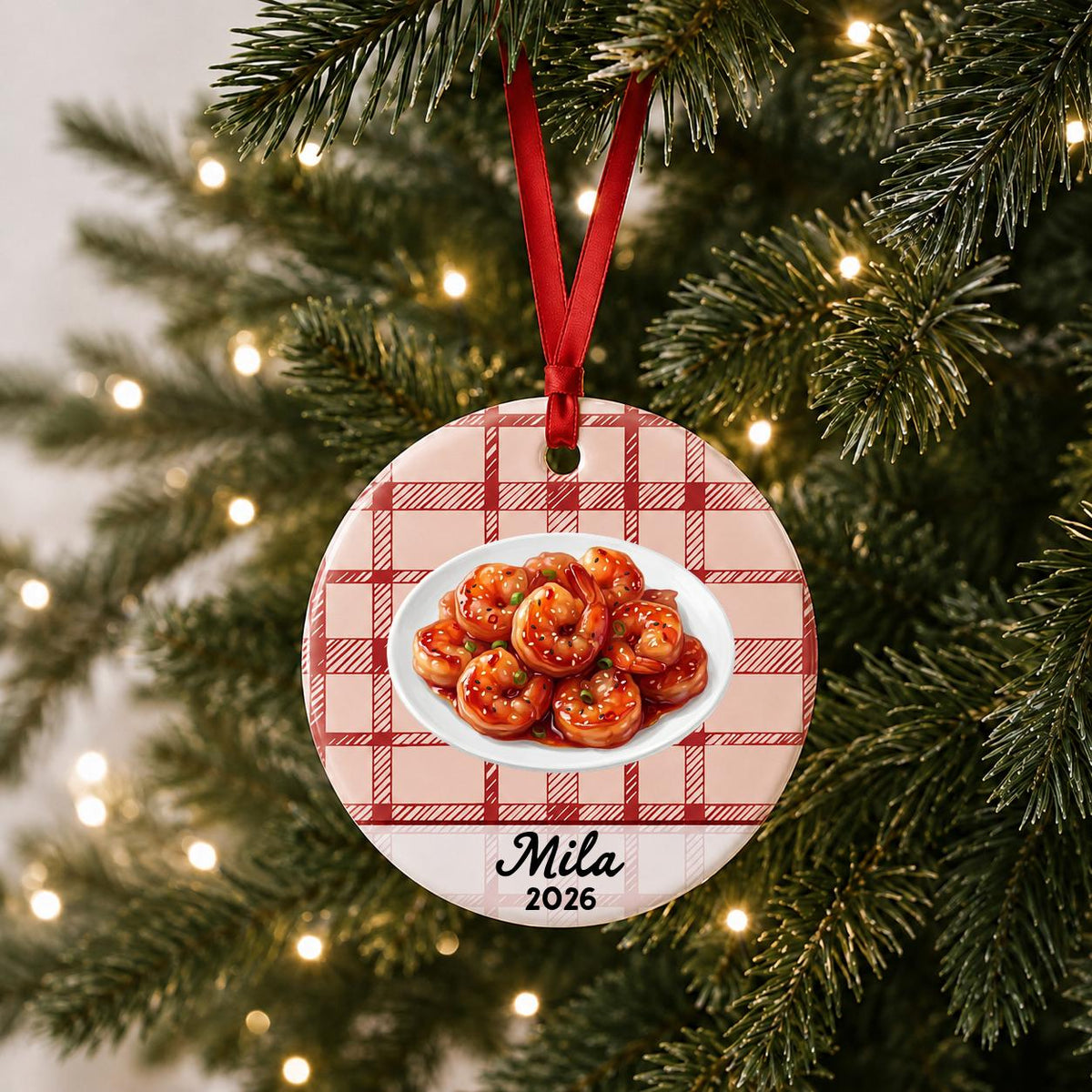 Personalized sesame shrimp ceramic ornament with name and year on red plaid hanging on a lit Christmas tree