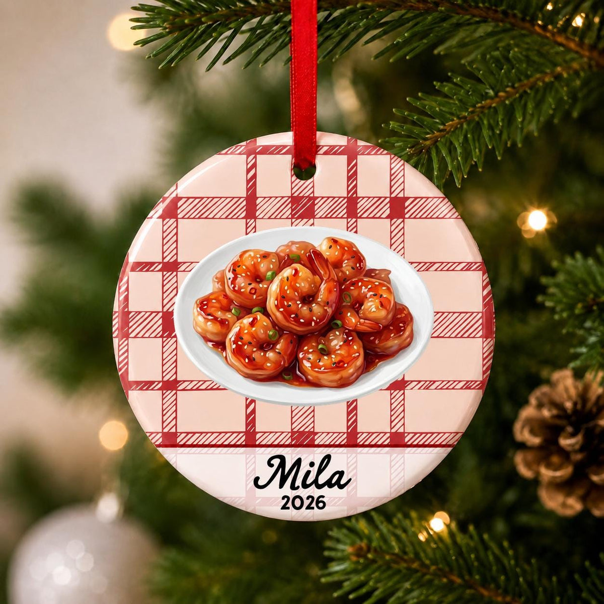 Close-up of the personalized sesame shrimp ceramic ornament with name and year on red plaid hanging on a Christmas tree